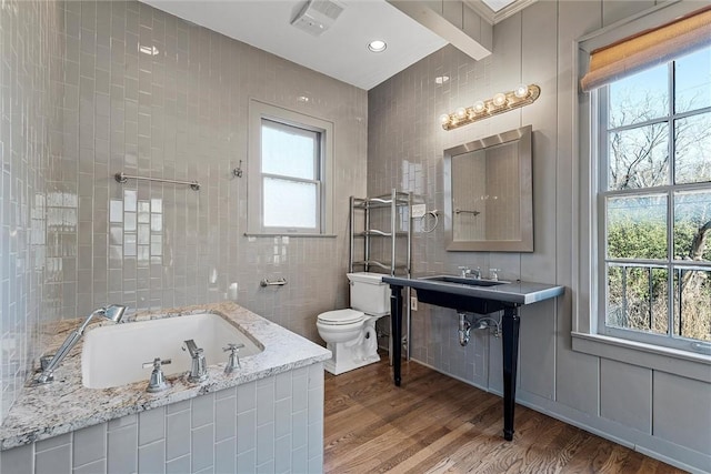 3100 Austin Ave, Waco, TX 76710 - bathroom featuring toilet, tile walls, tiled tub, wood finished floors, and vanity