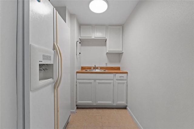 3100 Austin Ave, Waco, TX 76710 - kitchen featuring a sink, white refrigerator with ice dispenser, light tile patterned flooring, white cabinets, and baseboards