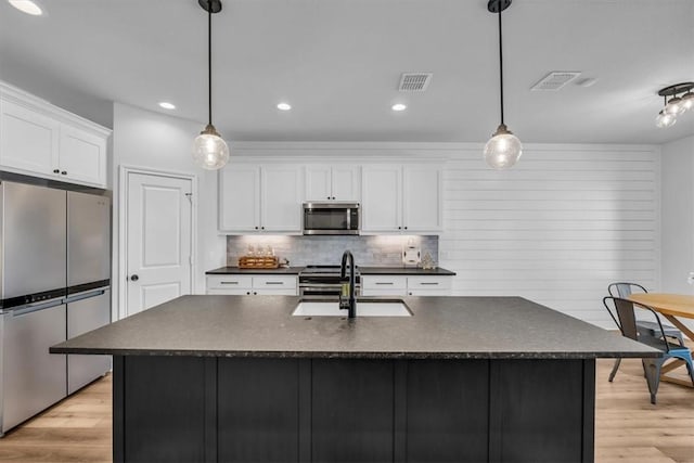 kitchen with a sink, stainless steel appliances, dark countertops, and visible vents