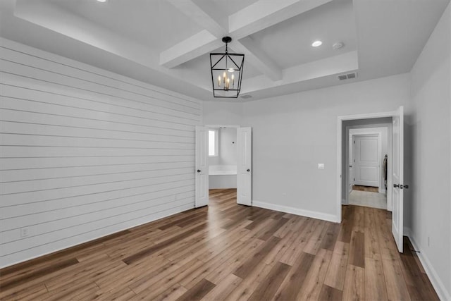 empty room featuring visible vents, a notable chandelier, coffered ceiling, wood finished floors, and baseboards