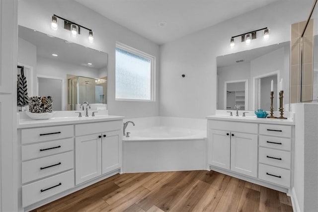 full bathroom featuring a stall shower, two vanities, a garden tub, and wood finished floors