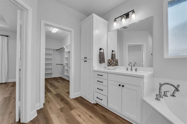 full bathroom with a walk in closet, visible vents, wood finished floors, a bath, and vanity