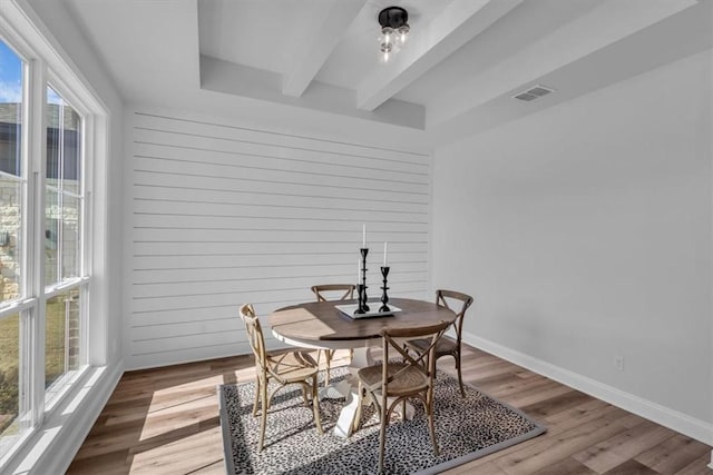 dining area featuring beam ceiling, visible vents, wood walls, and wood finished floors