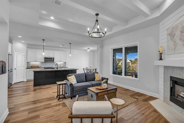 living area featuring visible vents, baseboards, light wood-style floors, and beam ceiling