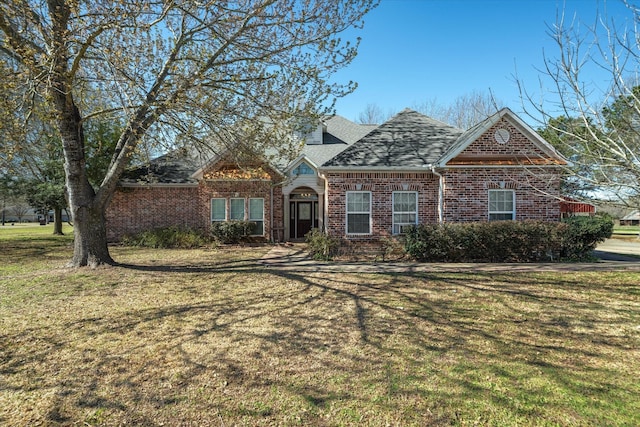 traditional-style home with a front yard, brick siding, and roof with shingles