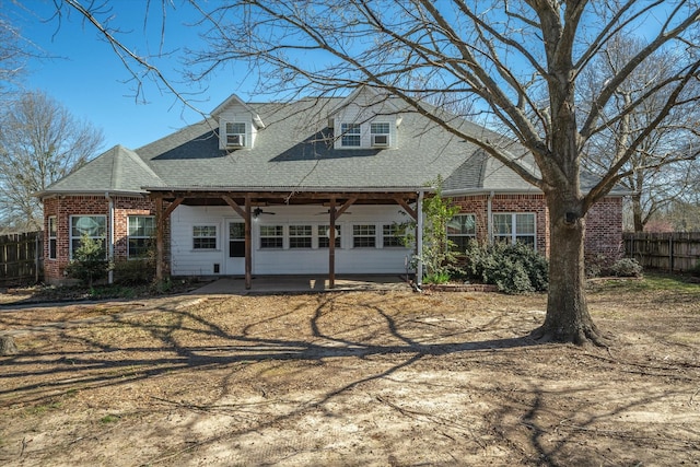 cape cod home featuring brick siding, a shingled roof, ceiling fan, and fence