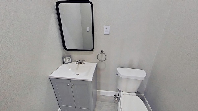 half bathroom featuring baseboards, vanity, toilet, and a textured wall