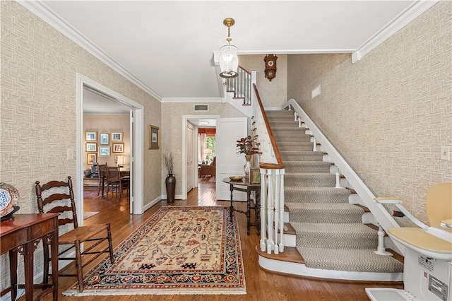 foyer entrance with ornamental molding, wallpapered walls, stairs, and wood finished floors