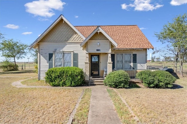 bungalow-style home with roof with shingles, a front lawn, and fence