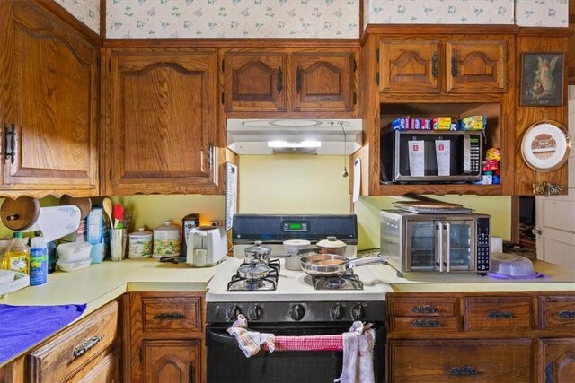 kitchen with under cabinet range hood, gas stove, wallpapered walls, and light countertops