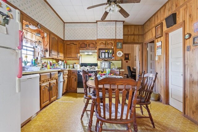 dining space with wooden walls, light floors, wallpapered walls, and a ceiling fan