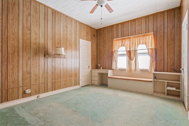 empty room featuring carpet flooring, wood walls, and ceiling fan