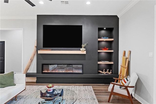 living area featuring visible vents, built in shelves, ornamental molding, wood finished floors, and a glass covered fireplace