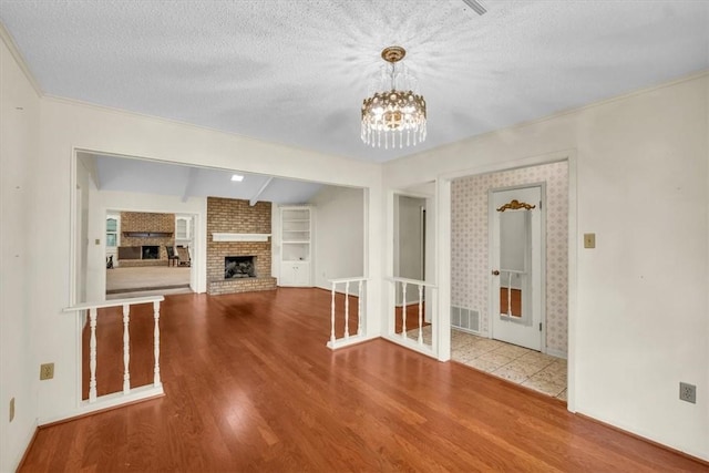 unfurnished living room with a notable chandelier, built in shelves, a textured ceiling, and wood finished floors
