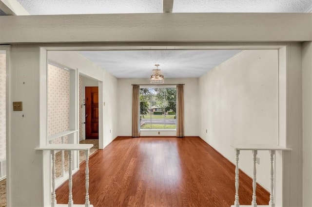 spare room featuring a textured ceiling, an inviting chandelier, and wood finished floors