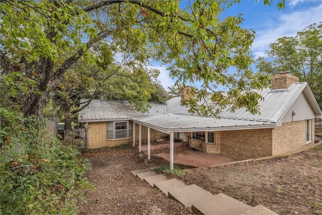 rear view of house featuring fence, metal roof, brick siding, a chimney, and a patio area