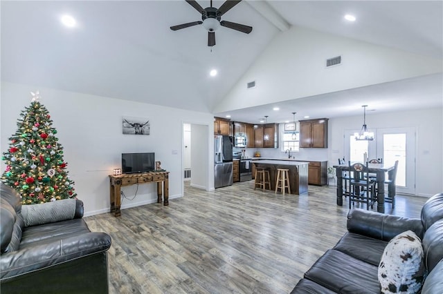 living room featuring visible vents, high vaulted ceiling, beam ceiling, ceiling fan with notable chandelier, and light wood-type flooring