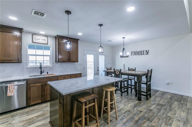 kitchen with wood finished floors, visible vents, a sink, stainless steel dishwasher, and tasteful backsplash