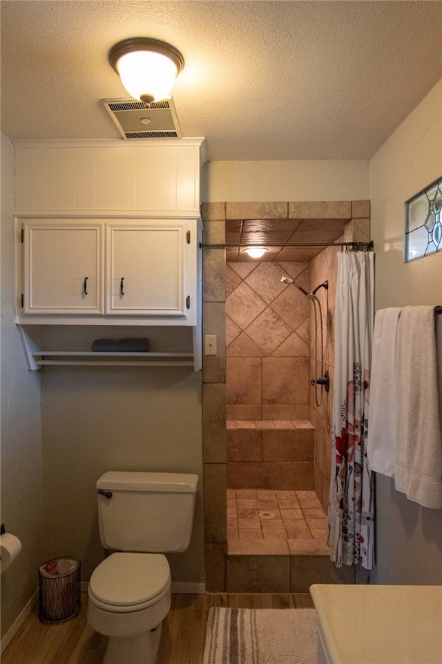 bathroom with visible vents, toilet, tiled shower, and wood finished floors
