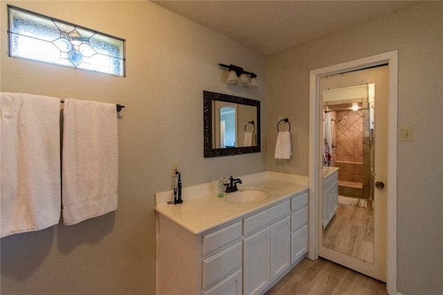 full bathroom featuring tiled shower, vanity, and wood finished floors