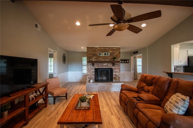 living room featuring visible vents, a brick fireplace, ceiling fan, vaulted ceiling, and light wood-style flooring