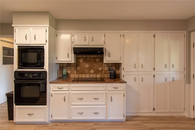 kitchen with tasteful backsplash, under cabinet range hood, light wood-type flooring, white cabinets, and black appliances