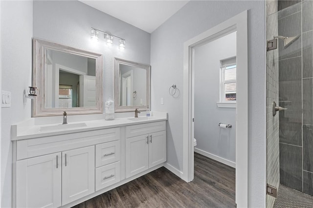 bathroom with wood finished floors, double vanity, a stall shower, a sink, and toilet