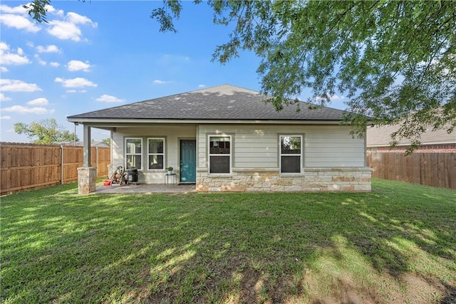 rear view of house featuring a yard, stone siding, and a fenced backyard