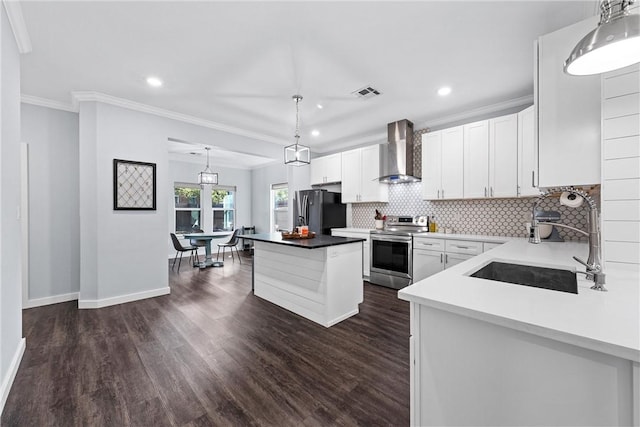 kitchen featuring visible vents, a center island, wall chimney range hood, stainless steel electric range, and freestanding refrigerator