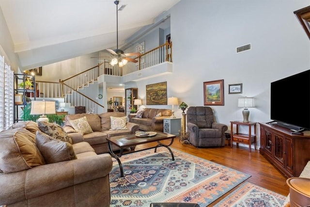 living area featuring visible vents, ceiling fan, stairs, a high ceiling, and wood finished floors