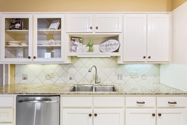 kitchen featuring light stone countertops, white cabinetry, a sink, glass insert cabinets, and dishwasher