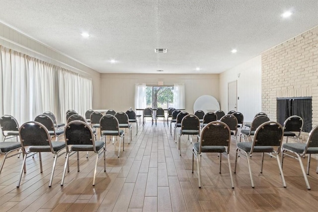 dining space with visible vents, a textured ceiling, a brick fireplace, and light wood-style flooring