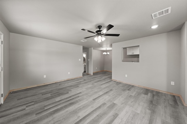 empty room featuring visible vents, light wood finished floors, ceiling fan with notable chandelier, and baseboards