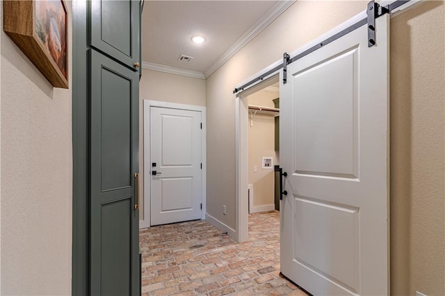 hall featuring visible vents, a barn door, crown molding, brick floor, and baseboards