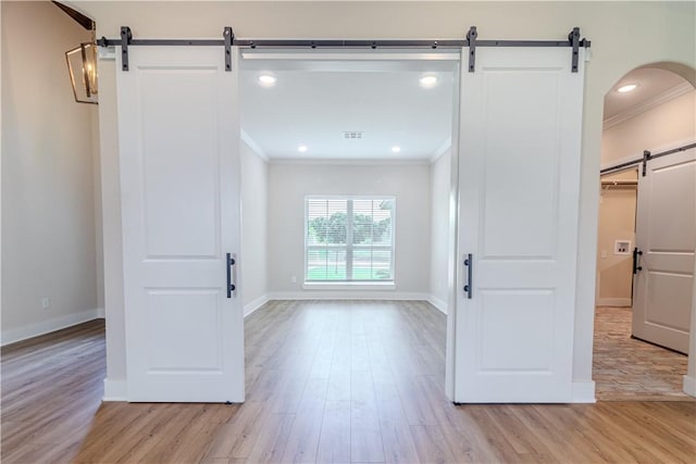 empty room with baseboards, recessed lighting, ornamental molding, light wood-style floors, and a barn door