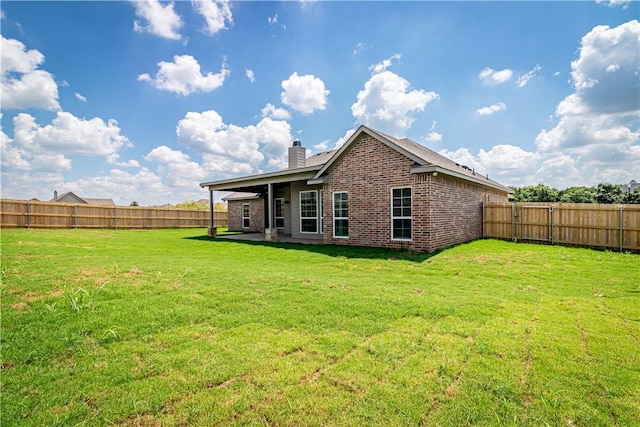 back of house with a lawn, brick siding, a fenced backyard, and a chimney