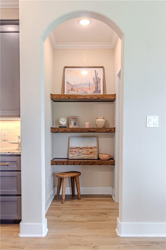 hall featuring crown molding, baseboards, arched walkways, and light wood-type flooring