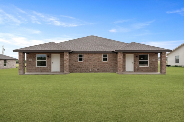 back of house featuring a yard, brick siding, a shingled roof, and a patio