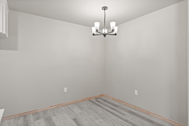 unfurnished room featuring an inviting chandelier, baseboards, and light wood-type flooring