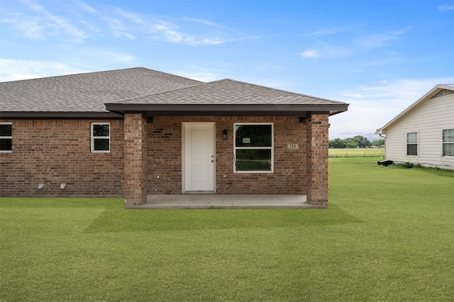 rear view of property with brick siding, a shingled roof, a lawn, and a patio