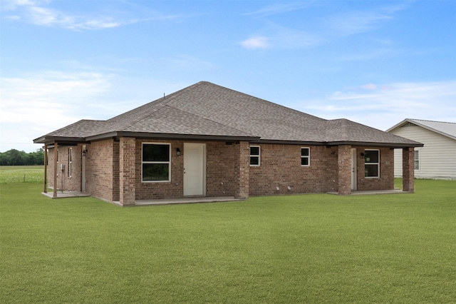 back of property with a lawn, brick siding, a patio area, and roof with shingles