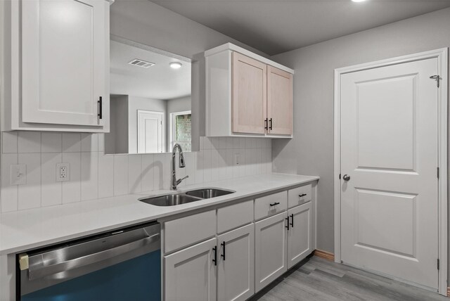 kitchen with tasteful backsplash, dishwasher, a sink, light countertops, and light wood finished floors