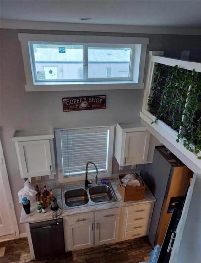 kitchen featuring light countertops, dishwashing machine, a sink, and white cabinetry