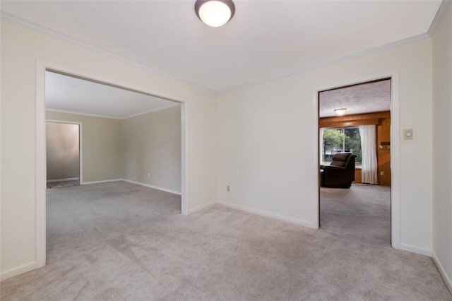 spare room featuring light carpet, crown molding, and baseboards