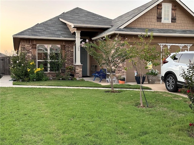 view of front of property featuring driveway, an attached garage, a shingled roof, a front lawn, and brick siding