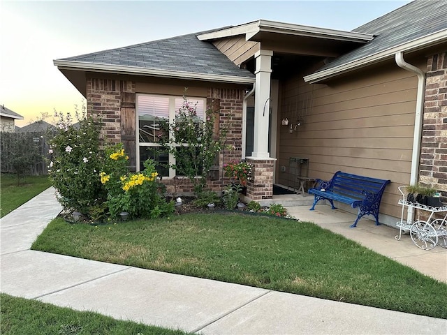 entrance to property featuring a yard, brick siding, and roof with shingles