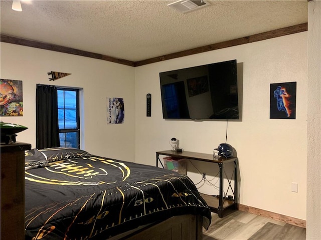 bedroom featuring wood finished floors, baseboards, visible vents, a textured ceiling, and crown molding