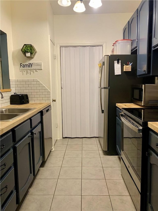 kitchen featuring tasteful backsplash, butcher block counters, light tile patterned flooring, stainless steel appliances, and a sink