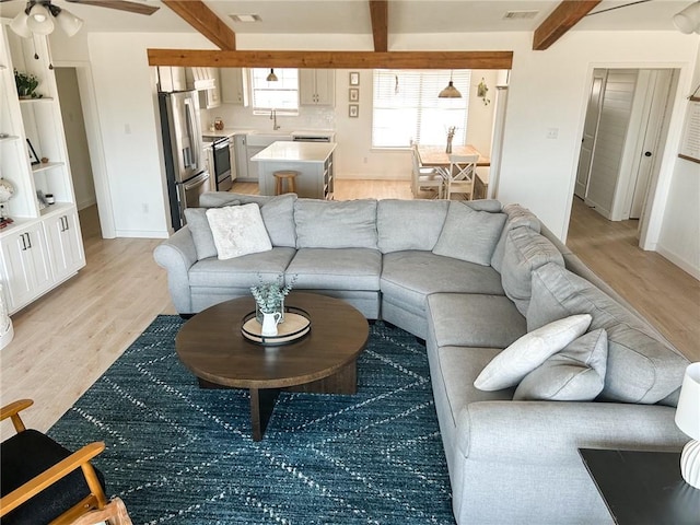 living room featuring light wood-type flooring, beamed ceiling, visible vents, and ceiling fan