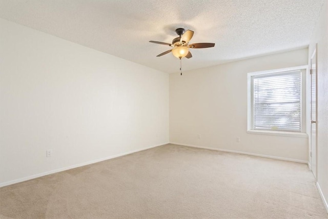 spare room with ceiling fan, baseboards, a textured ceiling, and light colored carpet